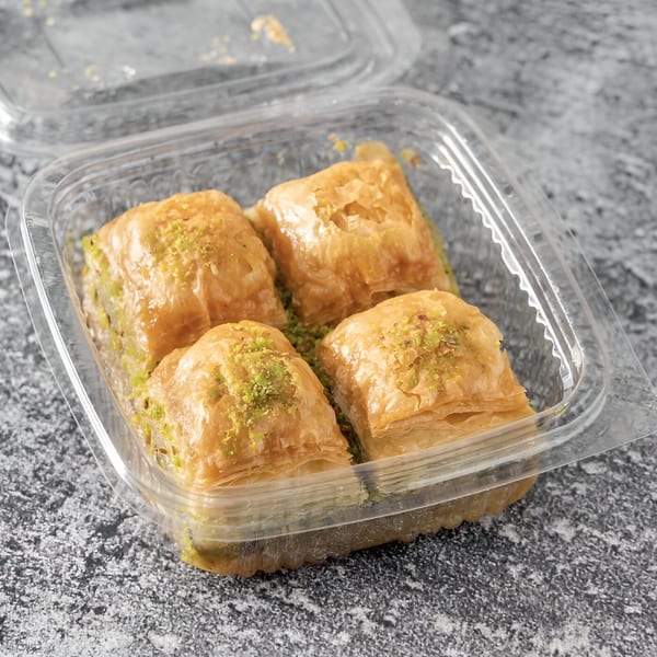 Four pieces of golden baklava with pistachio sprinkles in a clear plastic container.