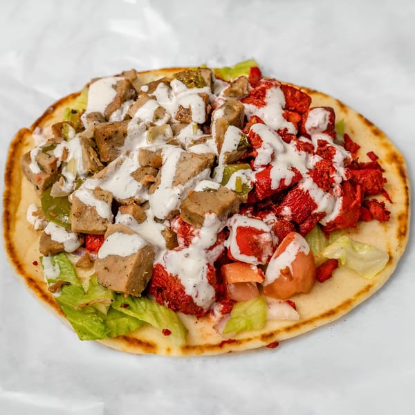Halal Haven's chicken and lamb gyro, topped with white sauce, lettuce, and tomatoes on pita bread.